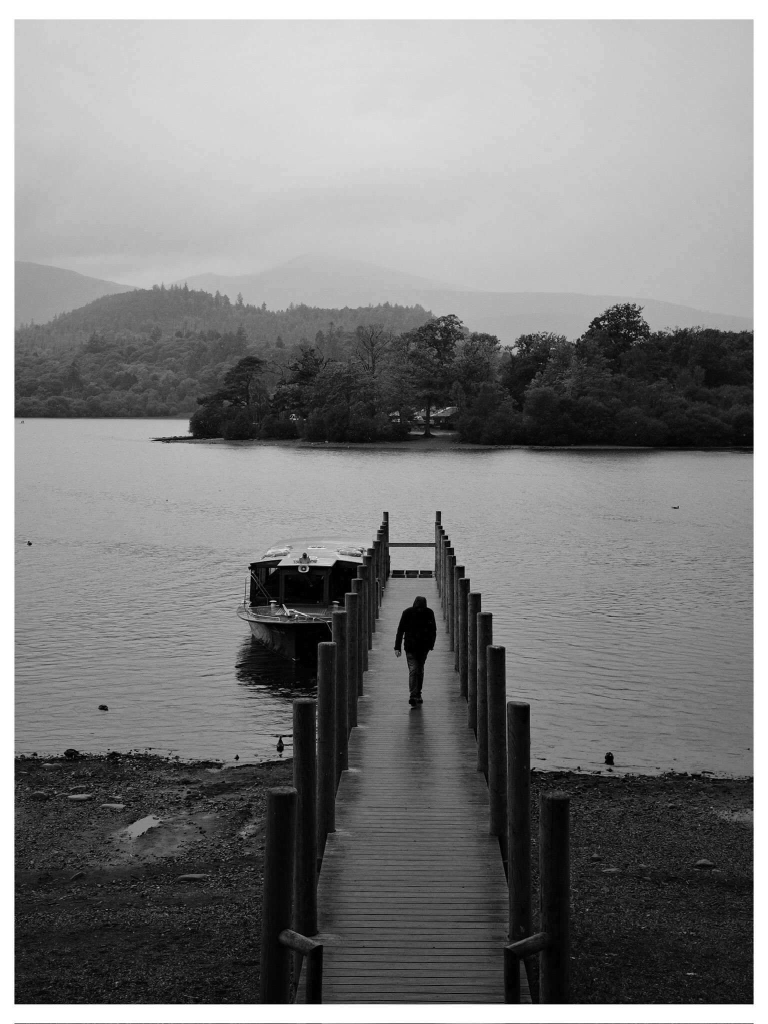 Black-and-white view along a jetty towards a lake and hills